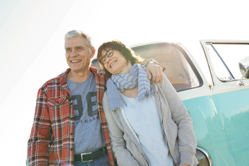Cheerful senior couple standing in front of camper van