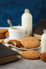 A cup of Coffee, Cookies, Raisins, Bottles with Milk, Oat Flakes and Books. Breakfast Concept