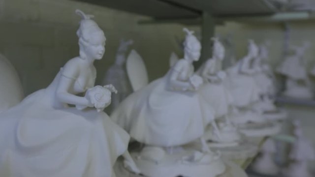 A lot of white porcelain figures of girls with a bouquet in a porcelain workshop.