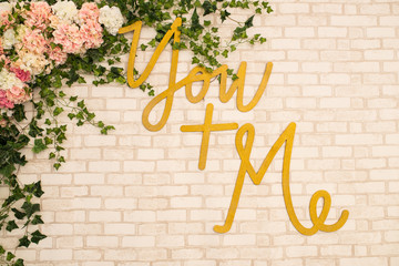 Brick background with the inscription “You + me” and a lot of flowers. Decoration.