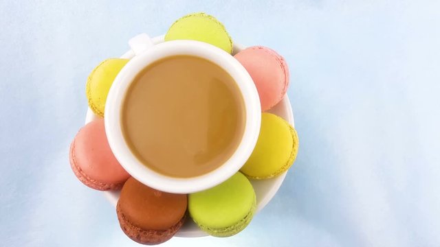 Macaroons or macaron on pastel pink surface with coffee in white cup.