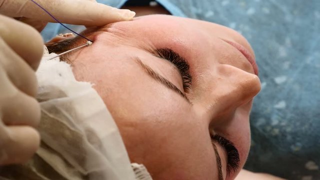 Healtcare clinic. Young female client gets thread face lifting procedure. Beautician in gloves making face anti-aging to a female face