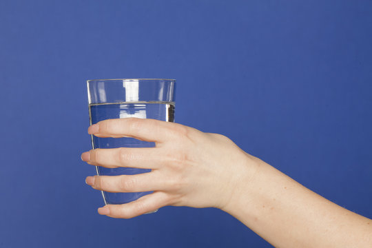 Female hand holding a glass of water on blue background