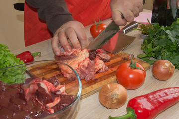 a man in a kitchen apron, meat on a board and a wooden table, a knife and vegetables