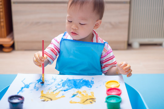 Cute smiling little Asian 18 months / 1 year old toddler baby boy child finger painting with hands and watercolors, kid painting at home, Creative play for kids and toddlers concept