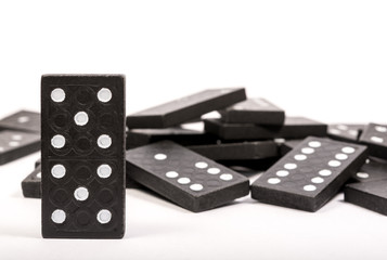 One black wooden domino chain standing before fallen dominoes on a white background. Logical Game. Business concept. Space for text.