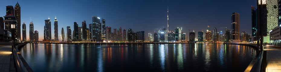 Panoramic view of Business bay skyline with reflection in the water at night, Dubai, UAE