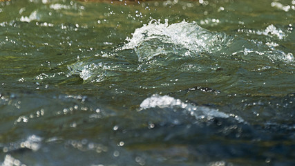 Fast mountain stream splashing and flowing over rocks on a bright sunny day