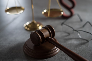 Law and Justice concept. Mallet of the judge, glasses, scales of justice. Gray stone background, reflections on the floor, place for typography. Courtroom theme.