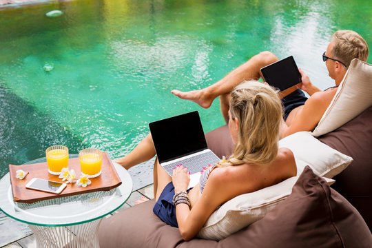 Couple chilling by the pool and working on computers