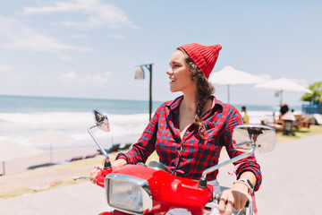 Hipster pretty lady dressed in plaid shirt and red cap drives on the red bike in sunlight on...