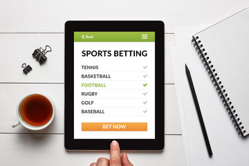 Sports betting concept on tablet screen with office objects on white wooden table. All screen content is designed by me. Flat lay