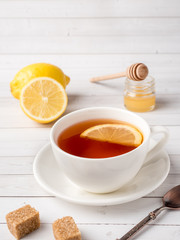 Herbal black tea in a white Cup, honey in a jar of fresh lemon on white wooden background