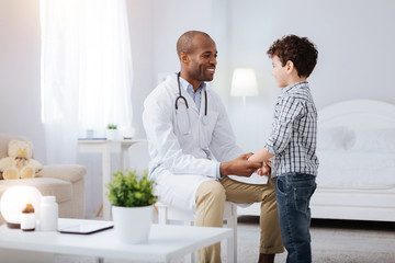 Obraz premium Trust me. Jolly happy male doctor smiling and taking hands of boy who staying in front of him
