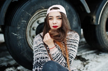 Brunette stylish casual girl in cap sitting against truck wheels.