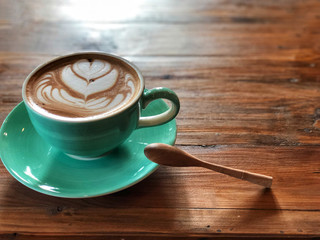 Latte art coffee in green cup and wooden spoon on the wooden table with natural light. Vintage style .