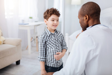 Obraz premium Discomfort in stomach. Glad positive boy grinning and touching tummy while talking to male doctor