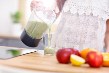 Fit smiling young woman preparing healthy smoothie in modern kitchen