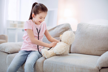 First patient. Happy jovial glad girl hearing plush bear while sitting on sofa and smiling