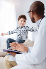 Obraz premium More details. Male doctor listening to energetic enthusiastic boy who smiling while holding clipboard