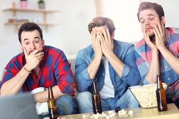 Sad male group of friends watching sports on tv at home