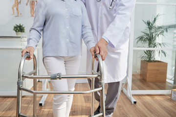 Close-up shot of unrecognizable physiotherapist explaining patient how to use front-wheeled walker,...