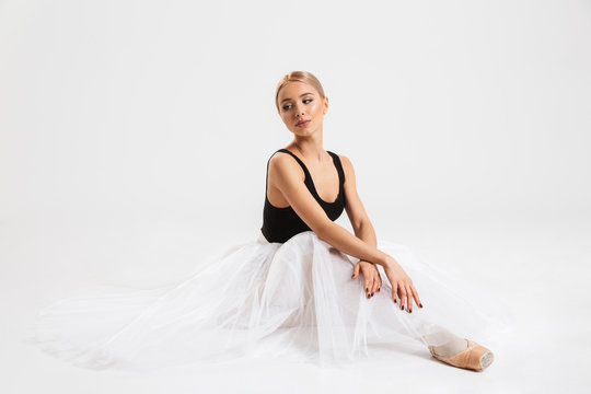 Amazing woman ballerina sitting over white wall