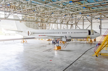 Passenger airplane on maintenance of engine, check repair in airport hangar. Aircraft side view, open hangar doors.