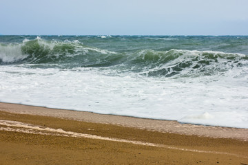Stormy sea and blue sky, white sea foam on a yellow sandy beach.