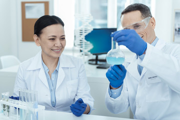 Best team. Attractive joyful smart experienced scientists smiling and wearing uniforms while making an experiment in the lab