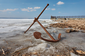 Rusty anchor on the frozen lake coast