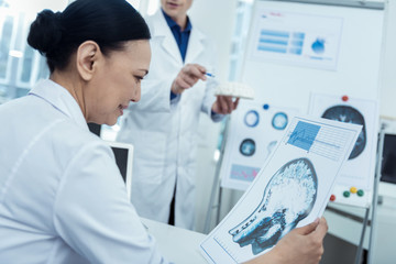 Check it up. Nice asian female doctor holding brain image while thinking out future surgery