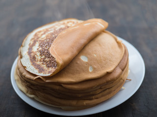 Stack of homemade pancakes on a white plate on a black background