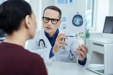 Explaining the problem. Professional therapeutist holdign a model of heart while having a check up