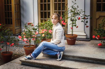 Obraz premium Young woman sits on the porch, terrace with access to the garden, among the roses