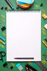 School supplies on green background. a blank Notepad in the frame of office supplies. copy space