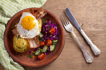 Baked potato in jacket loaded with cheese and topped with bacon and fried egg on plate with vegetables. Stuffed potato with topping. View from above, top, overhead