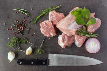 Fresh raw meat with herbs, spices and a butcher knife lies on the surface of a dark stone. Cooking concept.