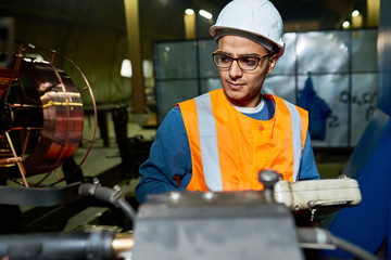 Portrait of modern young engineer wearing hardhat and glasses working at industrial plant