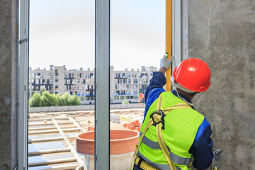 A worker in an orange helmet installs a double-glazed window in a new house, against a background...