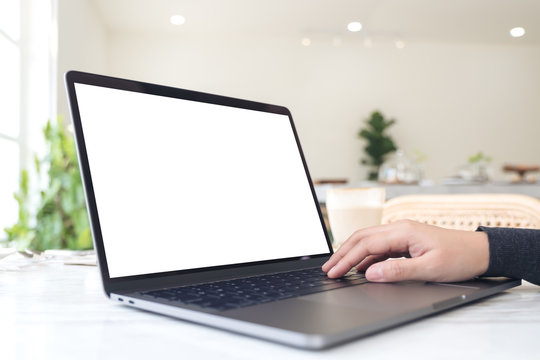 Mockup image of a hand typing and touching laptop with blank white desktop screen on table in cafe