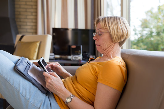 Older woman sitting on couch with tablet looking upset