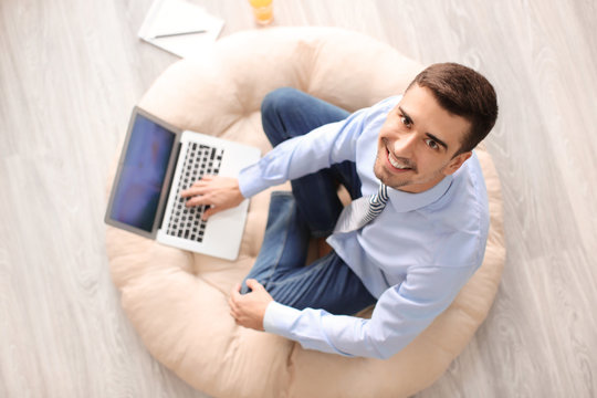 Young man with laptop sitting on floor at home, top view