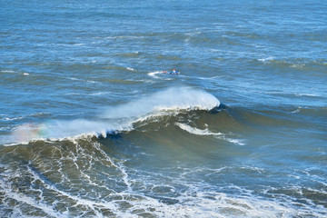 Fototapeta premium Two male surfers catch big wave at Nazare, safety team. Portugal