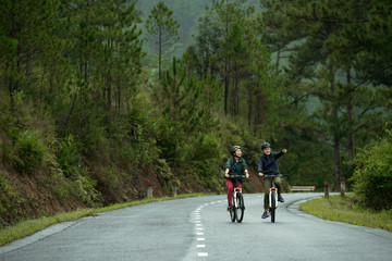 Asian couple cycling together down road, man pointing at something in the distance