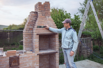 Adult man builds a brick oven and checks the wall with a half-barrel