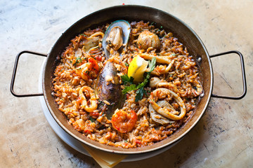 Paella Marinera Traditional, classic spanish main dish paella with shrimp mussels calamares white fish. Aged frying pan with rice, seafood lemon and herbs, up view selective focus.