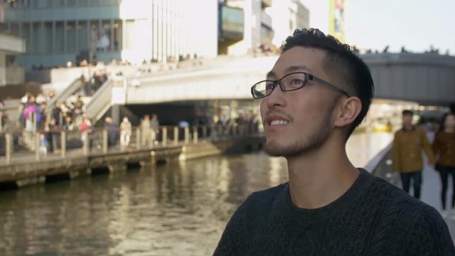 Asian man enjoying the sites in Japan by a busy cannal.
