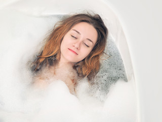 A young girl relaxes in the bath with foam