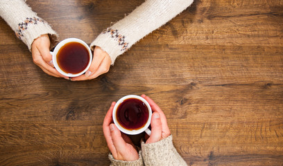 Cups of black tea in the hands of men and women. on a wooden background. with copy space. top view